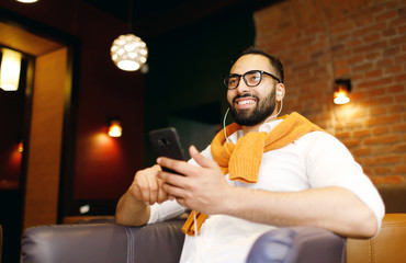 Portrait of a handsome man wearing glasses using smartphone indoors in restaurant