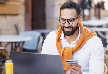 Portrait of masculine businessman in smiling and working on laptop while sitting in cafe outdoors