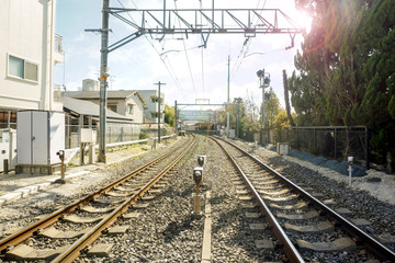 Fototapeta na wymiar Metal and stoneware railroad tracks and cityscape with sun flare and blurry background of crowd people waiting train at train platform.