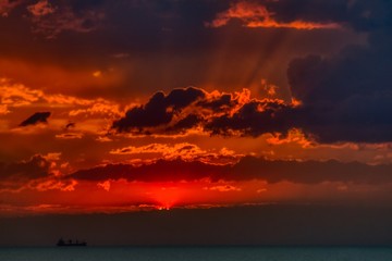 ship sailing at sunset, dramatic clouds, sun rays breaking through the clouds