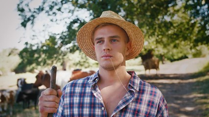 Portrait of young villager man shepherd in straw hat with his flock of cows on a rural background