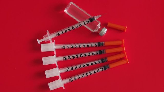 A lot of insulin syringes and an ampoule of hormone insulin on a red background, close-up. Diabetes. Disease. Background. The concept of health and medicine. Slow motion.