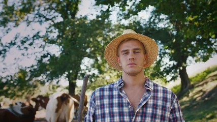 Portrait of young villager man shepherd in straw hat with his flock of cows on a rural background