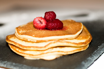 Pancakes with raspberries on black slate plate