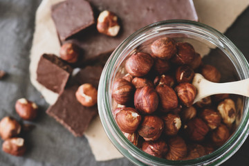 Dark chocolate and hazelnuts in a jar on a grey tablecloth background
