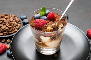 Classic tiramisu dessert portion with blueberries and raspberries in a glass cup on stone serving board on concrete background