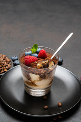 Classic tiramisu dessert portion with blueberries and raspberries in a glass cup on stone serving board on concrete background