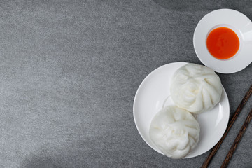 Chinese steamed buns and chilli sauce in white dish on concrete table.