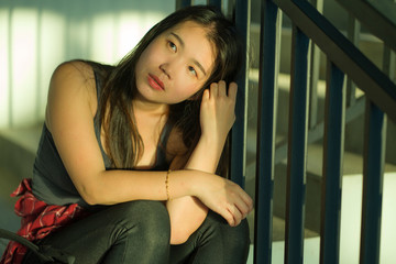 Young beautiful depressed Asian Japanese college student sitting on staircase victim of abuse feeling scared and lonely being harassed and bullied