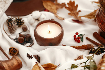 Hygge lifestyle. Candle, berries, fall leaves, herbs, acorns, nuts and brown hat on white fabric. Autumn mood. Hello autumn, cozy inspirational image.