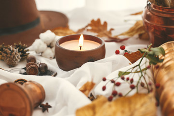 Fototapeta na wymiar Autumn mood. Candle, berries, fall leaves, herbs, acorns, nuts and brown hat on white fabric. Hello autumn, cozy inspirational image. Hygge lifestyle