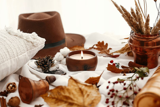 Hygge lifestyle. Candle, berries, fall leaves, herbs, acorns, nuts and brown hat on white fabric. Autumn mood. Hello autumn, cozy inspirational image.