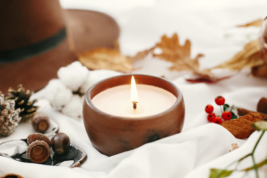 Hygge lifestyle. Candle, berries, fall leaves, herbs, acorns, nuts and brown hat on white fabric. Autumn mood. Hello autumn, cozy inspirational image.