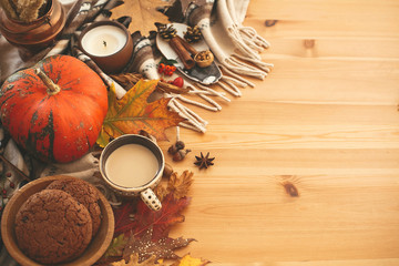 Coffee cup, candle,pumpkins with berries, fall leaves, anise,herbs, acorns, nuts, cinnamon, cotton on brown blanket, flat lay. Hygge lifestyle, cozy autumn mood.