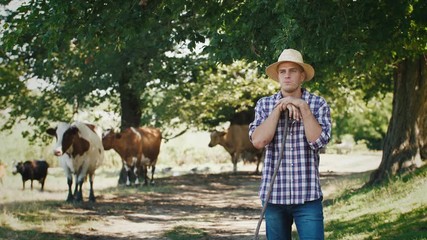 Young villager man shepherd in straw hat with his flock of cows on a rural background, slow motion