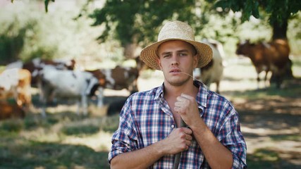Portrait of young villager man shepherd in straw hat with his flock of cows on a rural background
