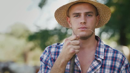 Portrait of young villager man shepherd in straw hat with his flock of cows on a rural background
