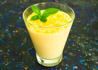 Vanilla mousse or pudding with lemon zest and mint in a glass tall glass on a dark blue background. Close-up.