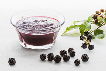 Glass pot of blackberry jam , blackberry bunch, white background