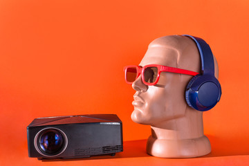 mannequin in blue headphones and red 3D glasses with a projector for home theater on orange...