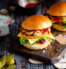 two homemade burgers with fried chicken, lettuce, cheese, onion, pickled cucumbers, ketchup