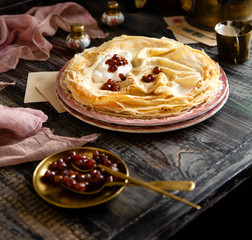 Homemade stack of thin crepes with sour cream and red jam on vintage pink plates