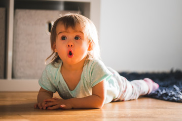 Adorable baby girl lying down on the carpet with funny expression