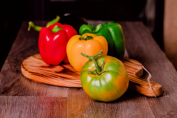 Pimientos verdes, rojos y amarillos sobre tabla de cortar junto a tomate verde y berenjena