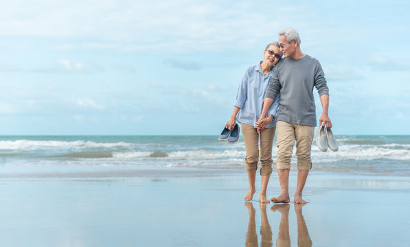 Age, Travel, Tourism and people concept - happy senior couple holding hands and walking on summer beach