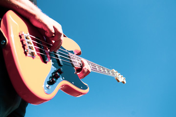 The guy plays an orange bass guitar against a cloudless blue sky
