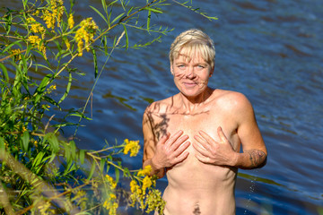 Attractive blonde naked woman comes out of the lake