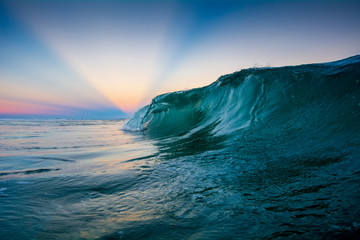 Sunset with sunrays behind a breaking wave at Campeche beach in Florianopolis Brazil