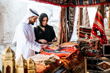 Happy couple spending time in Dubai. man and woman wearing traditional clothes making shopping in...