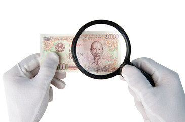 Hands in white gloves holding 2000 vietnamese dongs banknote investigeting counterfiet money with magnifier isolated on white background