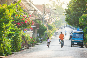 Father and daughter riding bicycle on the alley at dusk.