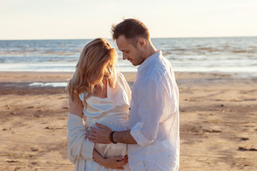 Love, waiting for the baby. Couple, pregnant woman and man, in white flying clothes, walk, hold hands, hug the tummy.