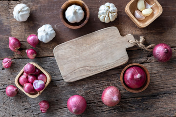 Top view of herbal vegetable ingredients, garlic, red onion, lime, lime leaf and chopping board on old wooden table, cooking preparation concept