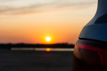 Dusty taillights of an off-road vehicle over background of a beach and water illuminated by the sun setting over the horizon.