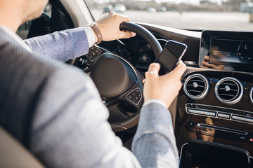 Young businessman looking at mobile phone while driving a car.
