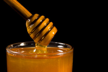 Honey jar with wooden spoon on black background. Closeup