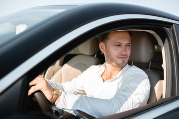 Portrait of a happy driver in a white shirt driving his luxary car.