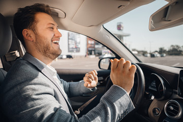 Happy driver in a suit dancing in his luxary car listening to music and enjouying life.
