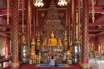 Fototapeta na wymiar nside a Buddhist temple in Thailand, chaired by a large golden Buddha, in the middle there is a tourist on her knees who takes pictures