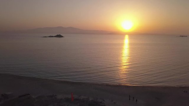 Drohnenflug in den Sonnenuntergang startend am Strand in Richtung Insel am Horizont