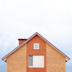 Fototapeta na wymiar Part of a red brick private building against a clear sky. Triangular roof and a window on the house. Copy space for articles on new affordable housing under the state program or mortgage lending.
