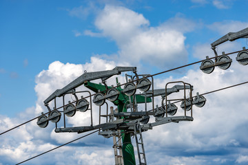 Close-up of a ski lift with a green pilon with steel cables and traction wheels, on blue sky with clouds. Italian Alps, Europe