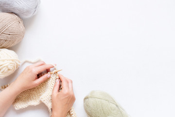 White background with knitting and female hands, balls of various pastel yarn and knitting process
