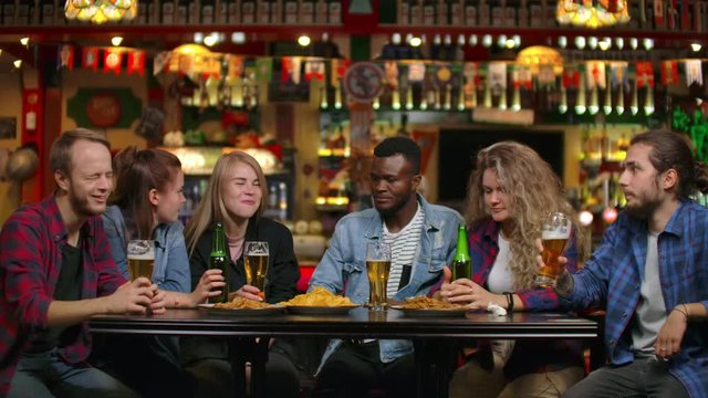 Multi-ethnic group of young men and women drinking beer at a bar and having a fun discussion about the university