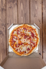 Italian pizza in cardboard box on wooden table. Top view