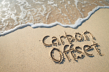 Carbon Offset message handwritten on smooth sand beach with incoming wave